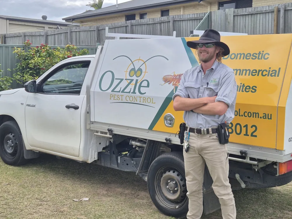 An Ozzie Pest Control technician in uniform standing beside a branded ute in a residential backyard